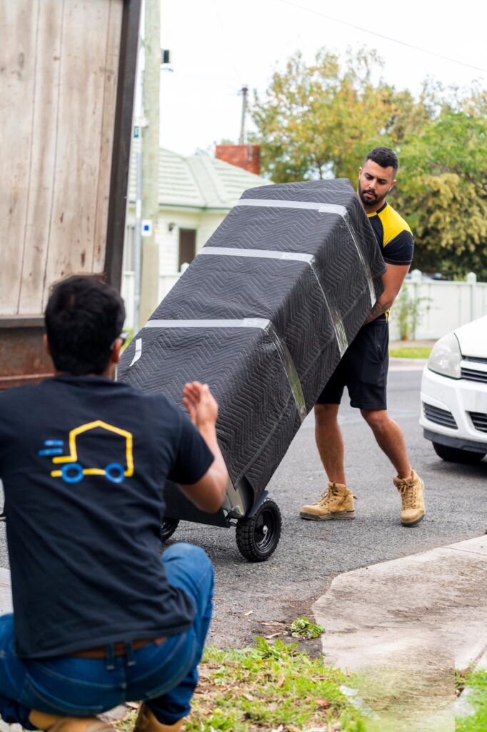 Removalists moving a large item wrapped in protective moving blankets, loading it safely into a truck