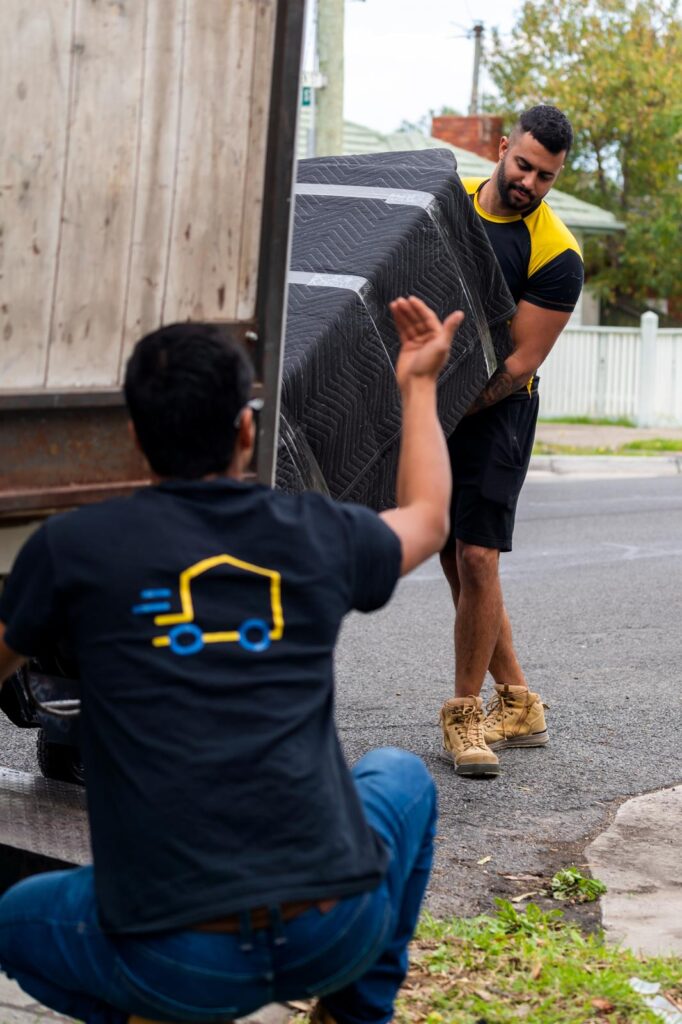 Removalists unloading a wrapped mattress from a moving truck for a residential move in Australia