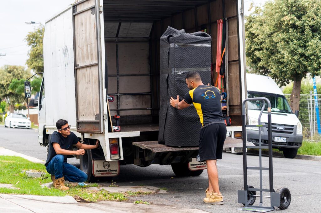 Removalists loading a large wrapped item onto a moving truck using a tail lift and dolly during a house move in Australia