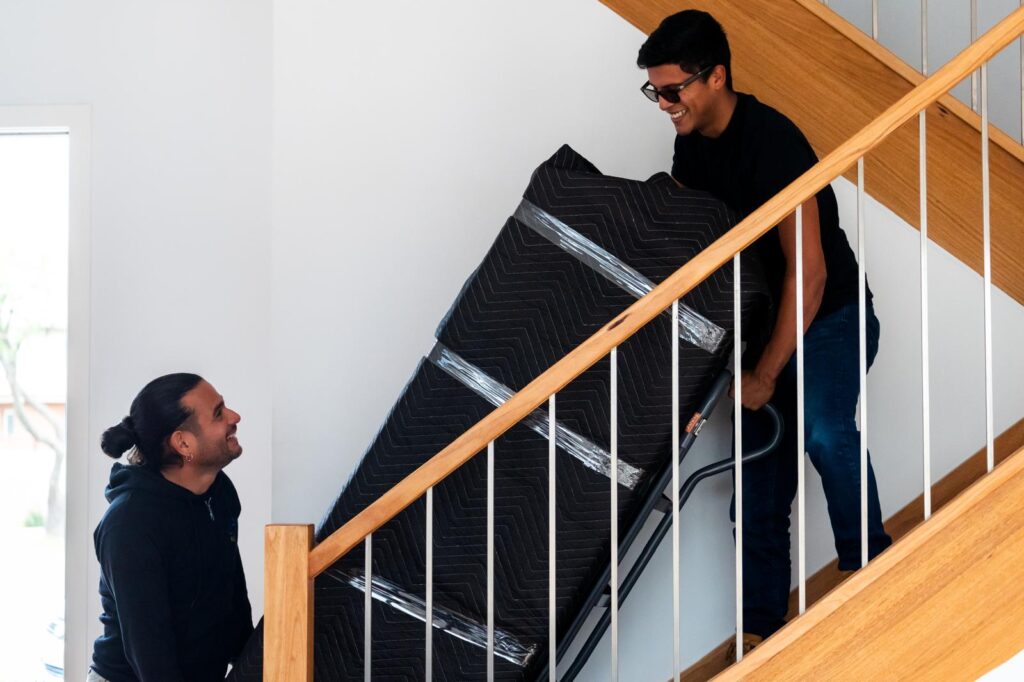 Removalists moving a large item up the stairs using a dolly and protective moving blankets