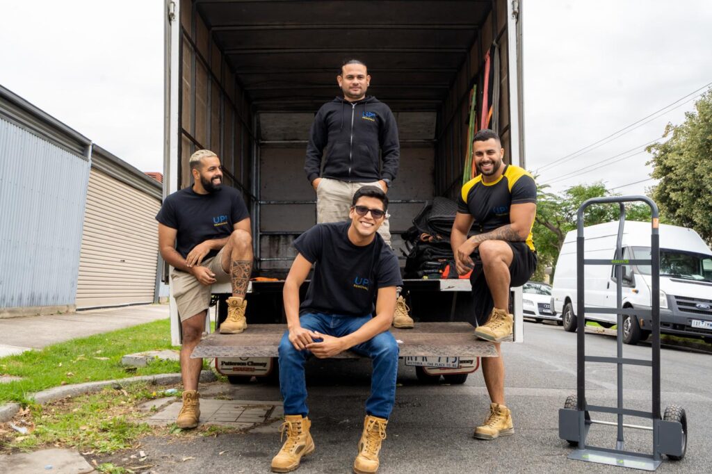 Professional removalists team posing on a moving truck tail lift with a dolly, ready for a house relocation in Australia
