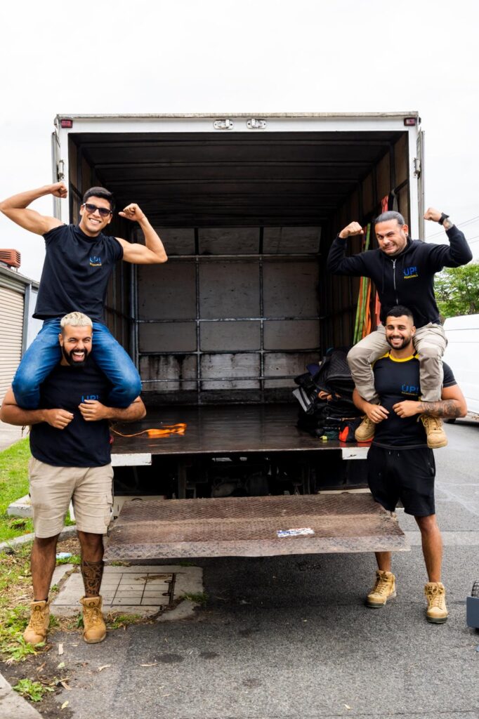 Removalists team posing and celebrating at the back of a moving truck during a home relocation